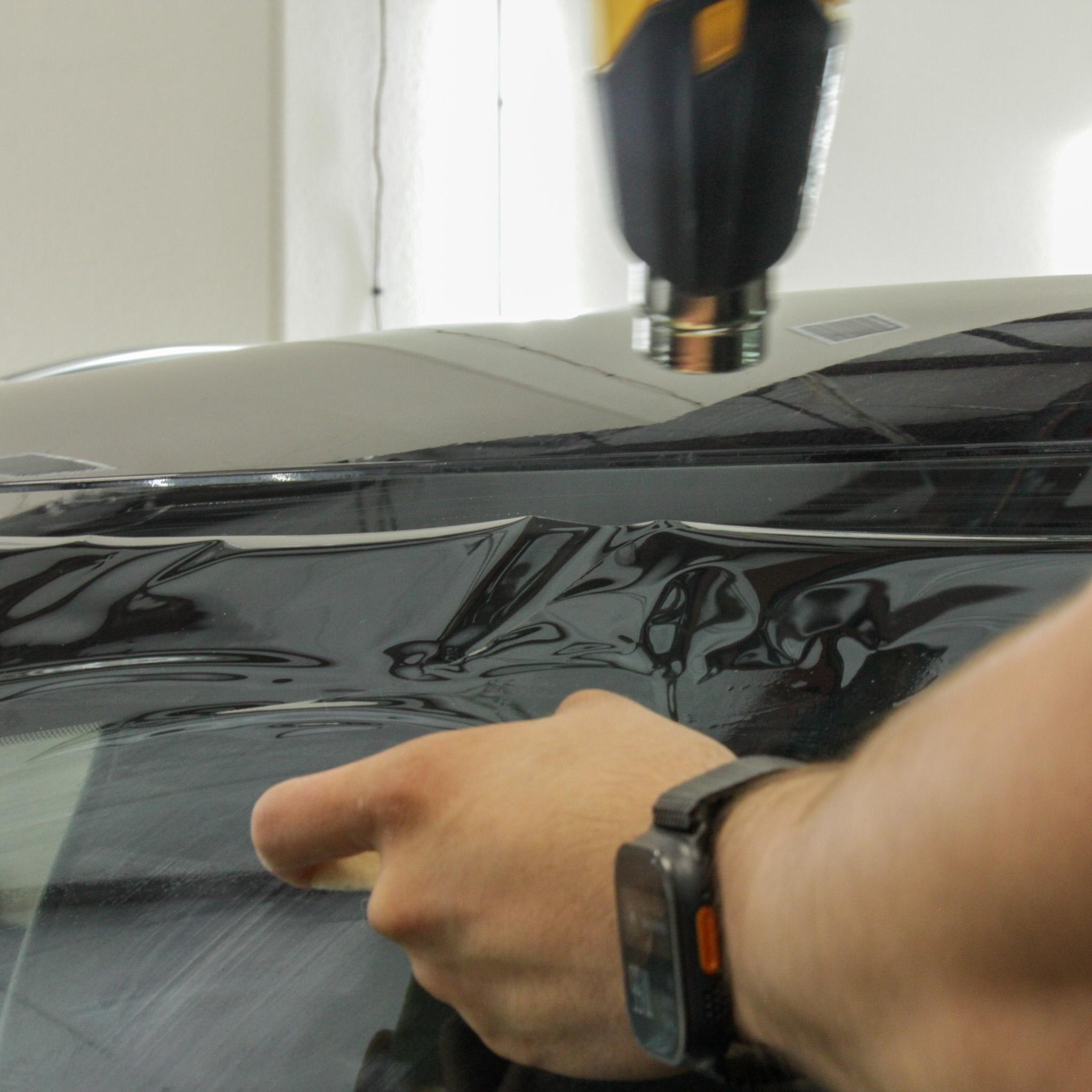 ### Main Subjects
- Person's hand
- Heat gun

### Objects
- Car window
- Window tint film

### Notable Features
- Application of window tint
- Use of a heat source to mold the film

### Text/Symbols
- None visible

### Overall Mood/Theme
The image conveys a sense of craftsmanship and attention to detail, showcasing the process of applying window tint to a car. The use of a heat gun suggests a methodical and professional approach, emphasizing the importance of precision in automotive detailing.